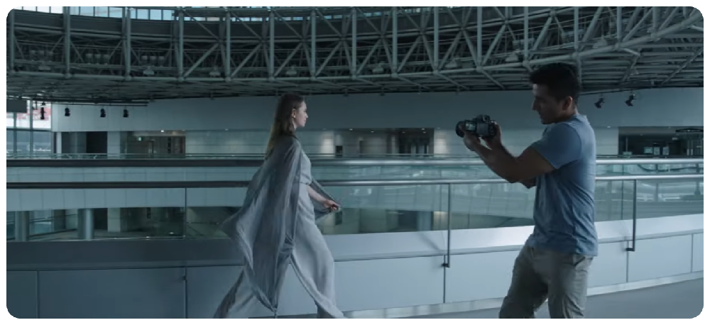 Sony A7 IV used by filmmaker recording woman walking through modern glass architecture building 